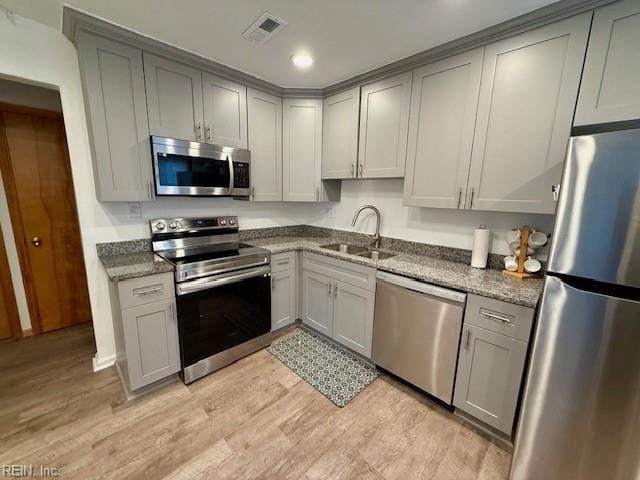 kitchen with gray cabinetry, dark stone counters, stainless steel appliances, sink, and light hardwood / wood-style floors