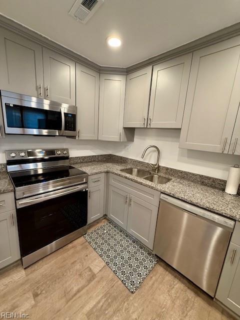 kitchen featuring gray cabinetry, sink, dark stone countertops, light wood-type flooring, and appliances with stainless steel finishes