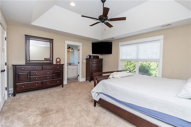 carpeted bedroom featuring ceiling fan, a tray ceiling, and ensuite bath