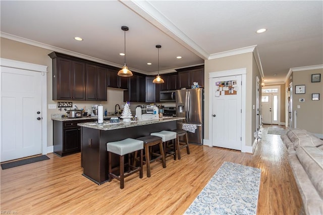 kitchen featuring stainless steel appliances, a kitchen island with sink, crown molding, decorative light fixtures, and light hardwood / wood-style flooring