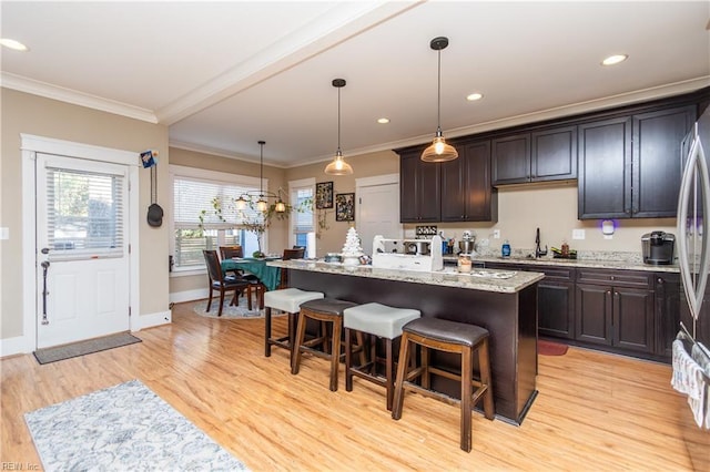 kitchen with a center island with sink, a kitchen breakfast bar, light hardwood / wood-style flooring, ornamental molding, and decorative light fixtures