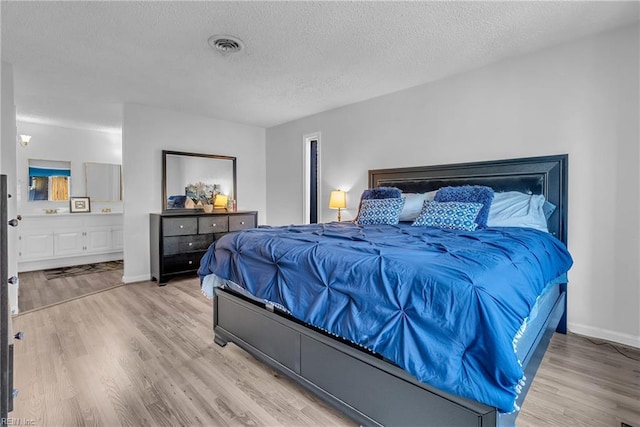 bedroom featuring ensuite bathroom, light wood-type flooring, and a textured ceiling