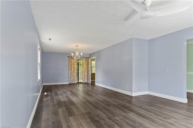 empty room featuring ceiling fan with notable chandelier and dark hardwood / wood-style floors