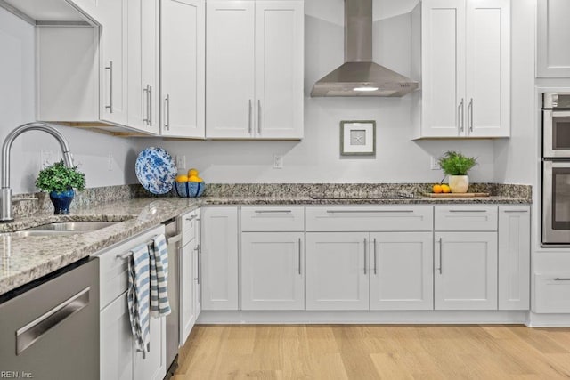 kitchen featuring sink, wall chimney exhaust hood, light wood-type flooring, white cabinetry, and stainless steel appliances