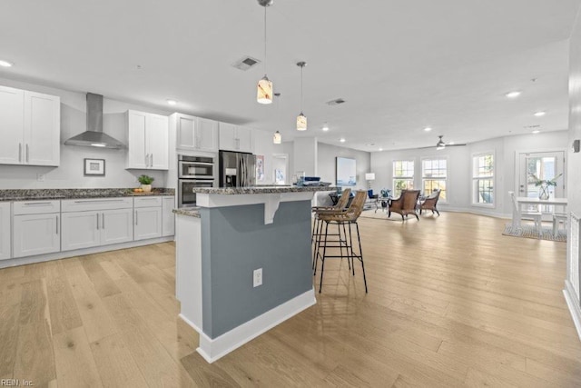 kitchen featuring a center island, wall chimney exhaust hood, stainless steel appliances, light hardwood / wood-style floors, and white cabinets