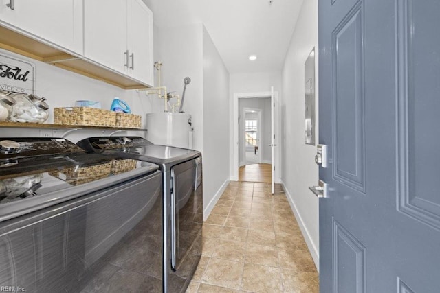 clothes washing area with water heater, washer and clothes dryer, and cabinets