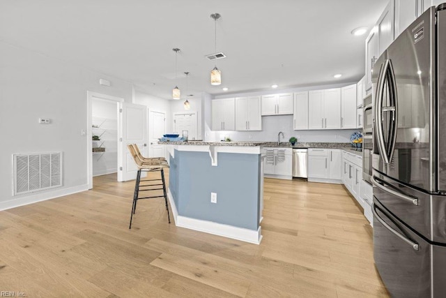 kitchen with white cabinetry, stainless steel appliances, pendant lighting, light hardwood / wood-style floors, and a kitchen island