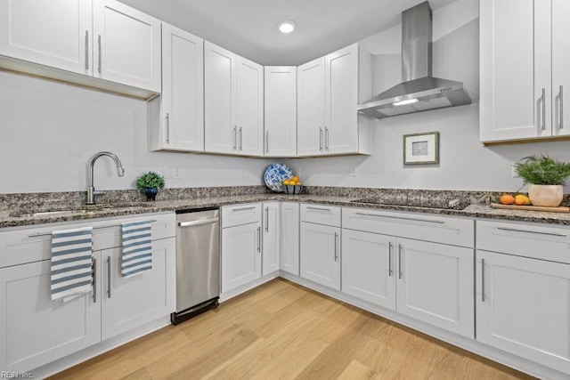 kitchen with white cabinetry, sink, wall chimney range hood, light hardwood / wood-style flooring, and dark stone counters