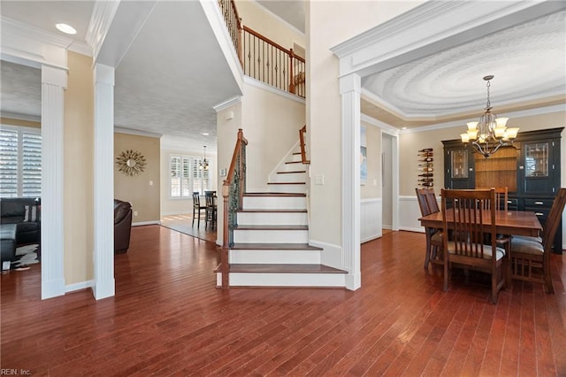 interior space featuring dark hardwood / wood-style floors, an inviting chandelier, ornamental molding, and ornate columns