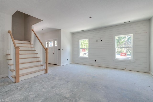 unfurnished living room with stairs, baseboards, and unfinished concrete floors