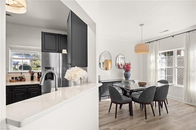 kitchen with sink, light hardwood / wood-style flooring, stainless steel fridge, decorative light fixtures, and light stone counters