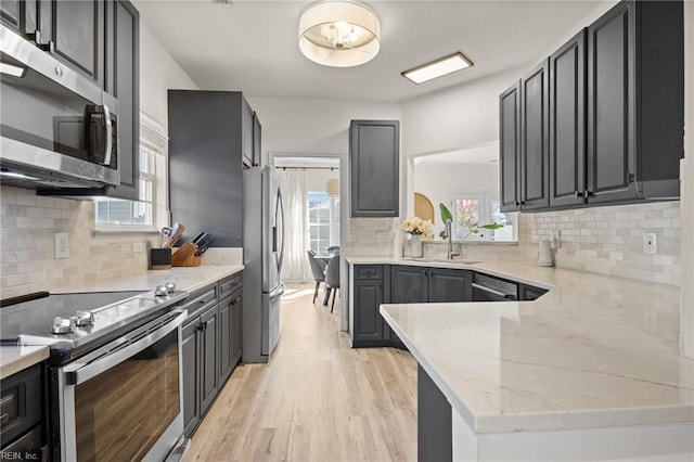 kitchen with light stone counters, plenty of natural light, stainless steel appliances, and light hardwood / wood-style floors