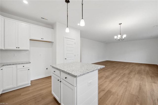 kitchen featuring light stone countertops, white cabinets, decorative light fixtures, and a kitchen island