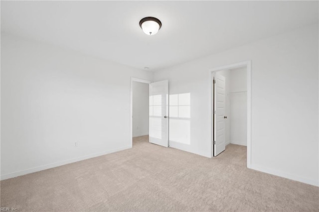 unfurnished bedroom with a spacious closet, a closet, and light carpet