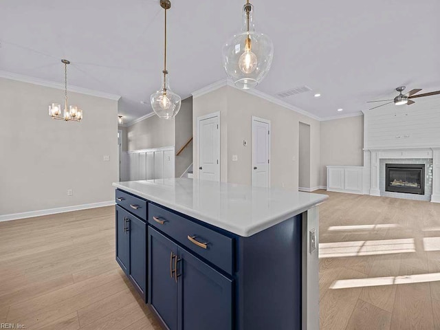 kitchen with blue cabinetry, a large fireplace, pendant lighting, light hardwood / wood-style floors, and a kitchen island