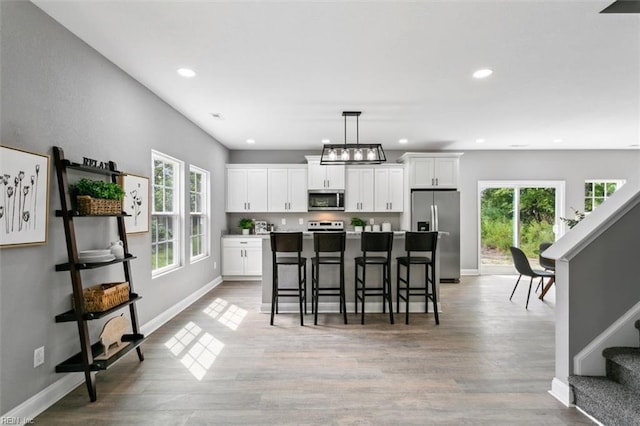 kitchen with a kitchen bar, appliances with stainless steel finishes, light wood-type flooring, white cabinets, and a center island