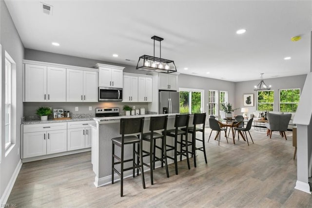 kitchen featuring a kitchen bar, white cabinetry, an island with sink, and appliances with stainless steel finishes