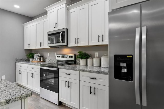 kitchen featuring light stone countertops, white cabinetry, appliances with stainless steel finishes, and light hardwood / wood-style flooring