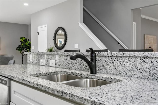 interior details featuring white cabinetry, light stone countertops, sink, stainless steel dishwasher, and ornamental molding