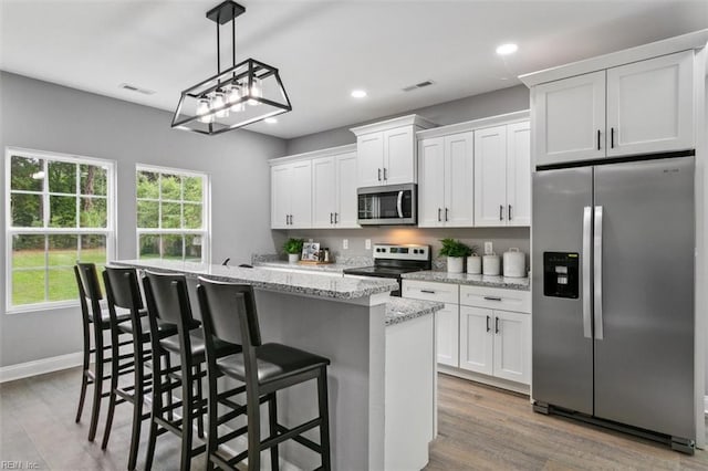 kitchen featuring white cabinets, appliances with stainless steel finishes, wood-type flooring, and an island with sink