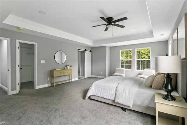 bedroom featuring a tray ceiling, a barn door, a spacious closet, and ceiling fan