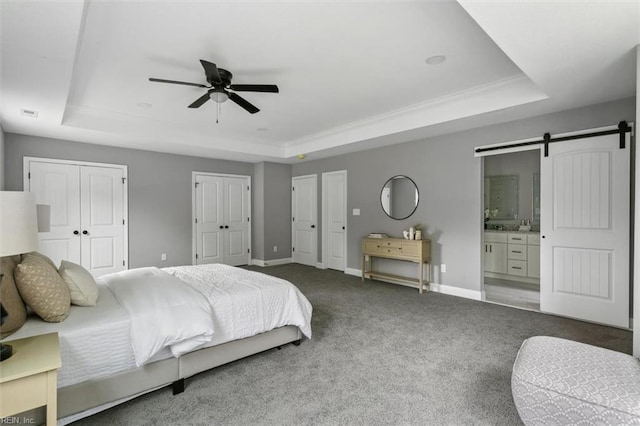 bedroom with a tray ceiling, a barn door, ceiling fan, and ensuite bath