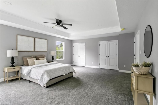 bedroom featuring dark colored carpet, a raised ceiling, ceiling fan, and multiple closets