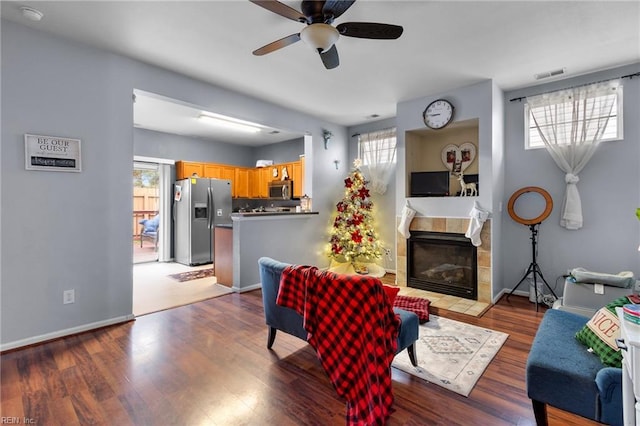 living room with ceiling fan, a tiled fireplace, and light wood-type flooring