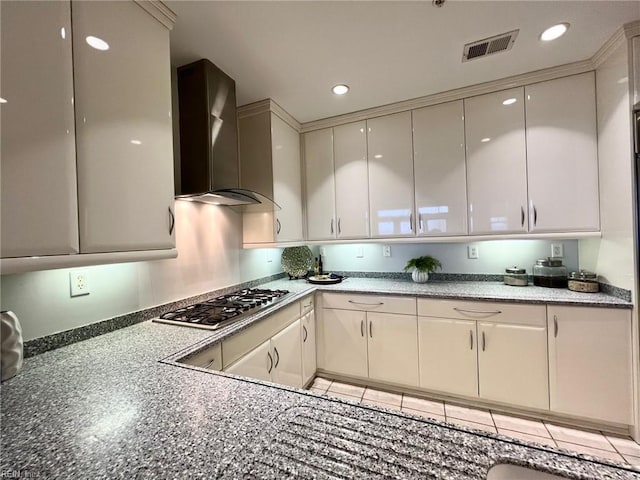 kitchen featuring light tile patterned floors, white cabinets, wall chimney range hood, and stainless steel gas cooktop