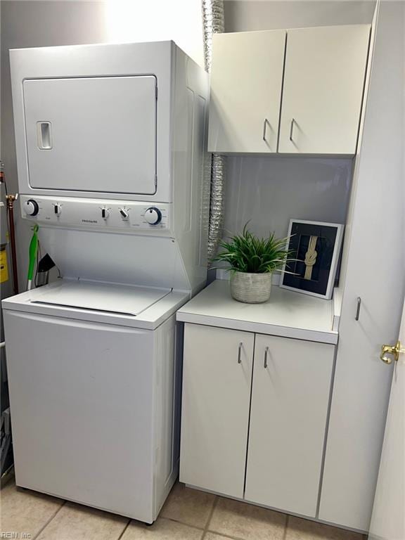 clothes washing area with light tile patterned flooring, cabinets, and stacked washing maching and dryer