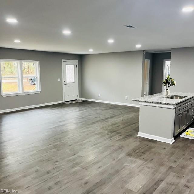 kitchen with sink, light stone counters, dark hardwood / wood-style flooring, an island with sink, and gray cabinets