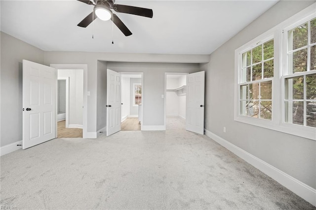 unfurnished bedroom with a walk in closet, ceiling fan, a closet, and light carpet