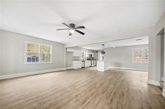 unfurnished living room with a wealth of natural light, light hardwood / wood-style flooring, ceiling fan, and beamed ceiling