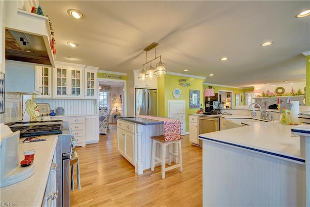 kitchen with white cabinets, decorative light fixtures, stainless steel appliances, and light hardwood / wood-style flooring