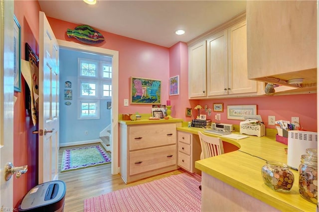 kitchen with light brown cabinets, built in desk, and light hardwood / wood-style floors