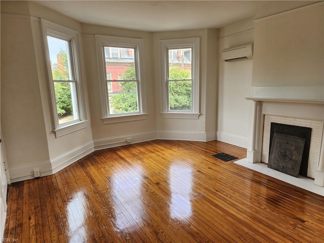 unfurnished living room with a wall mounted air conditioner, light wood-type flooring, a wealth of natural light, and a fireplace