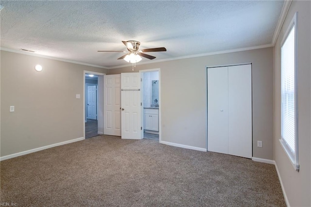 unfurnished bedroom featuring ensuite bath, ceiling fan, crown molding, carpet floors, and a textured ceiling