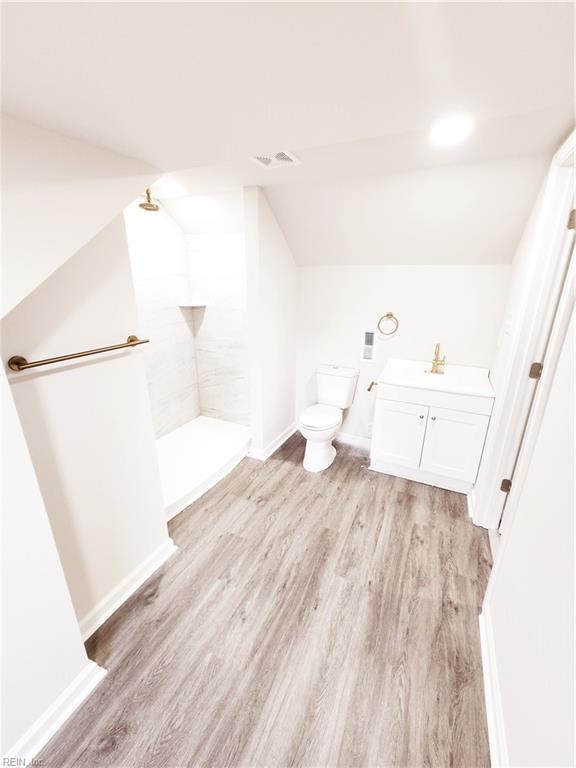 bathroom with hardwood / wood-style floors, vanity, vaulted ceiling, toilet, and walk in shower