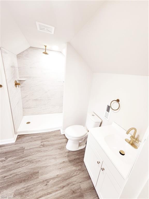 bathroom with wood-type flooring, vaulted ceiling, toilet, tiled shower, and vanity