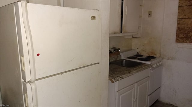 kitchen with white refrigerator, white cabinetry, and sink