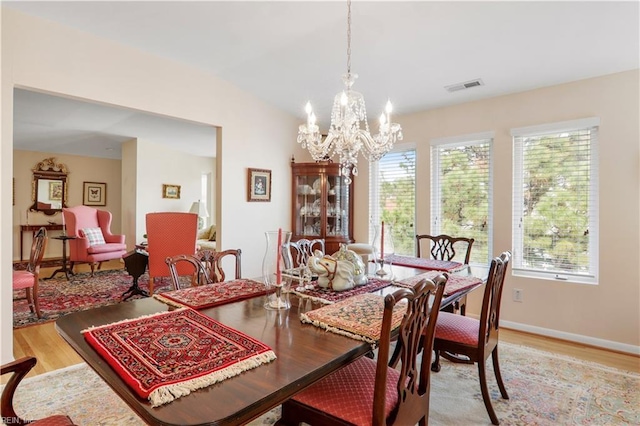 dining area with a notable chandelier, light hardwood / wood-style floors, and vaulted ceiling