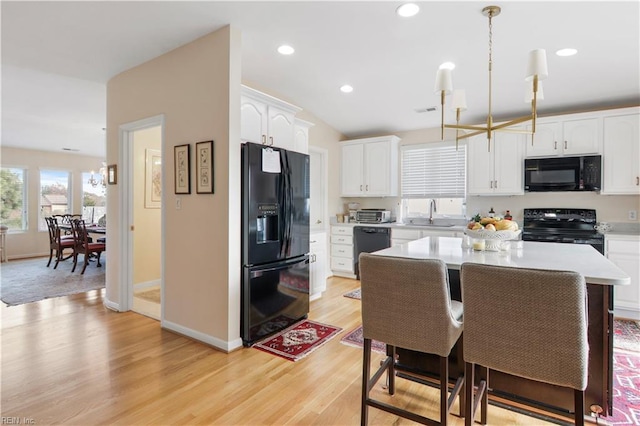 kitchen with pendant lighting, light hardwood / wood-style flooring, white cabinetry, and black appliances