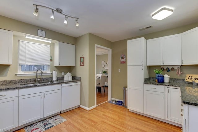 kitchen with light wood-type flooring, white cabinets, sink, dark stone countertops, and dishwasher