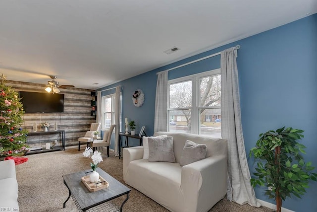 carpeted living room featuring ceiling fan and wooden walls