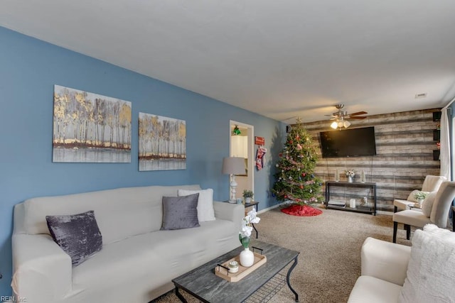 carpeted living room with ceiling fan and wood walls