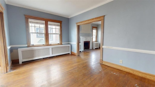 empty room featuring wood-type flooring, radiator heating unit, and crown molding