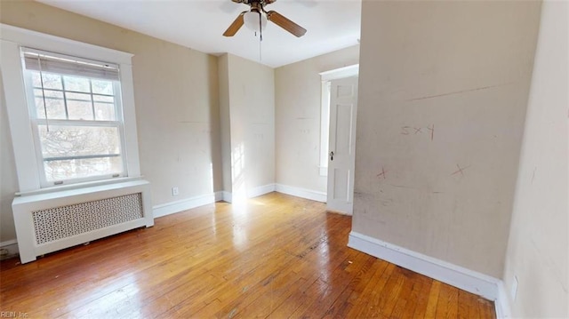 spare room featuring radiator heating unit, light hardwood / wood-style floors, and ceiling fan