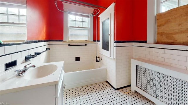 bathroom with vanity, a tub to relax in, radiator, and tile walls