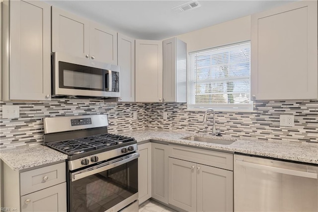 kitchen featuring tasteful backsplash, light stone countertops, sink, and appliances with stainless steel finishes