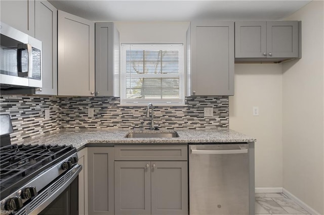 kitchen featuring tasteful backsplash, light stone counters, gray cabinetry, stainless steel appliances, and sink